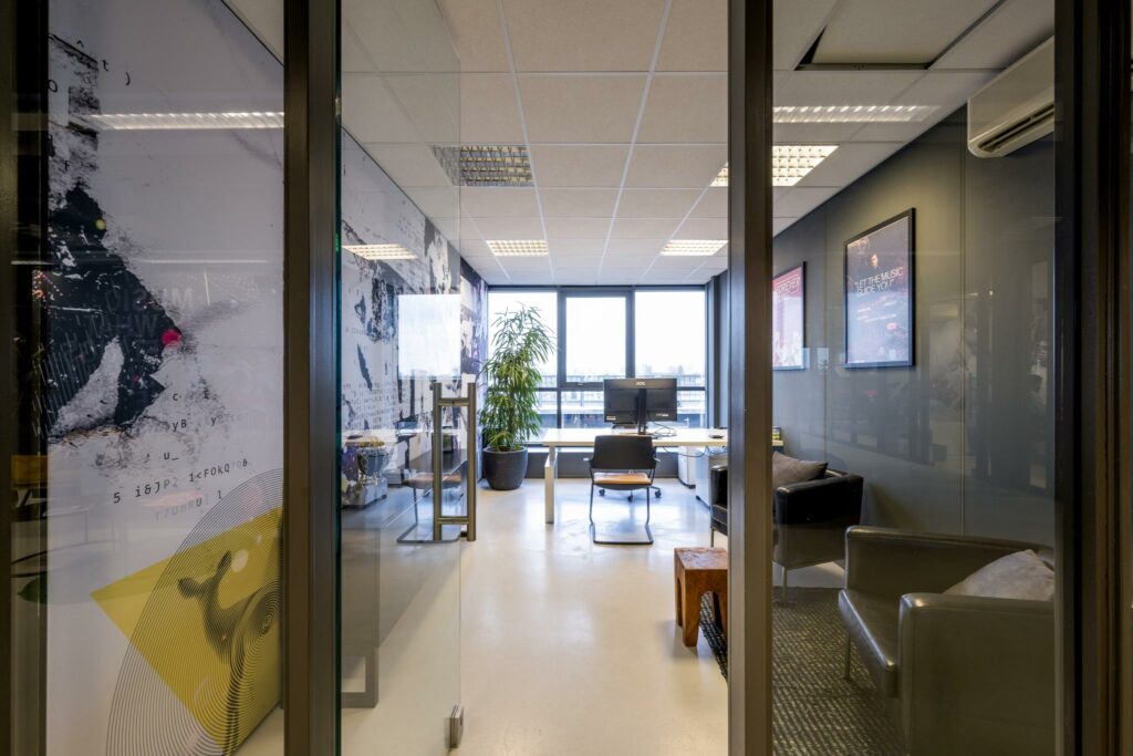 Modern kantoor aan de Anthony Fokkerweg met glazen wanden, bureaus, planten en muurbekleding met grafische prints.